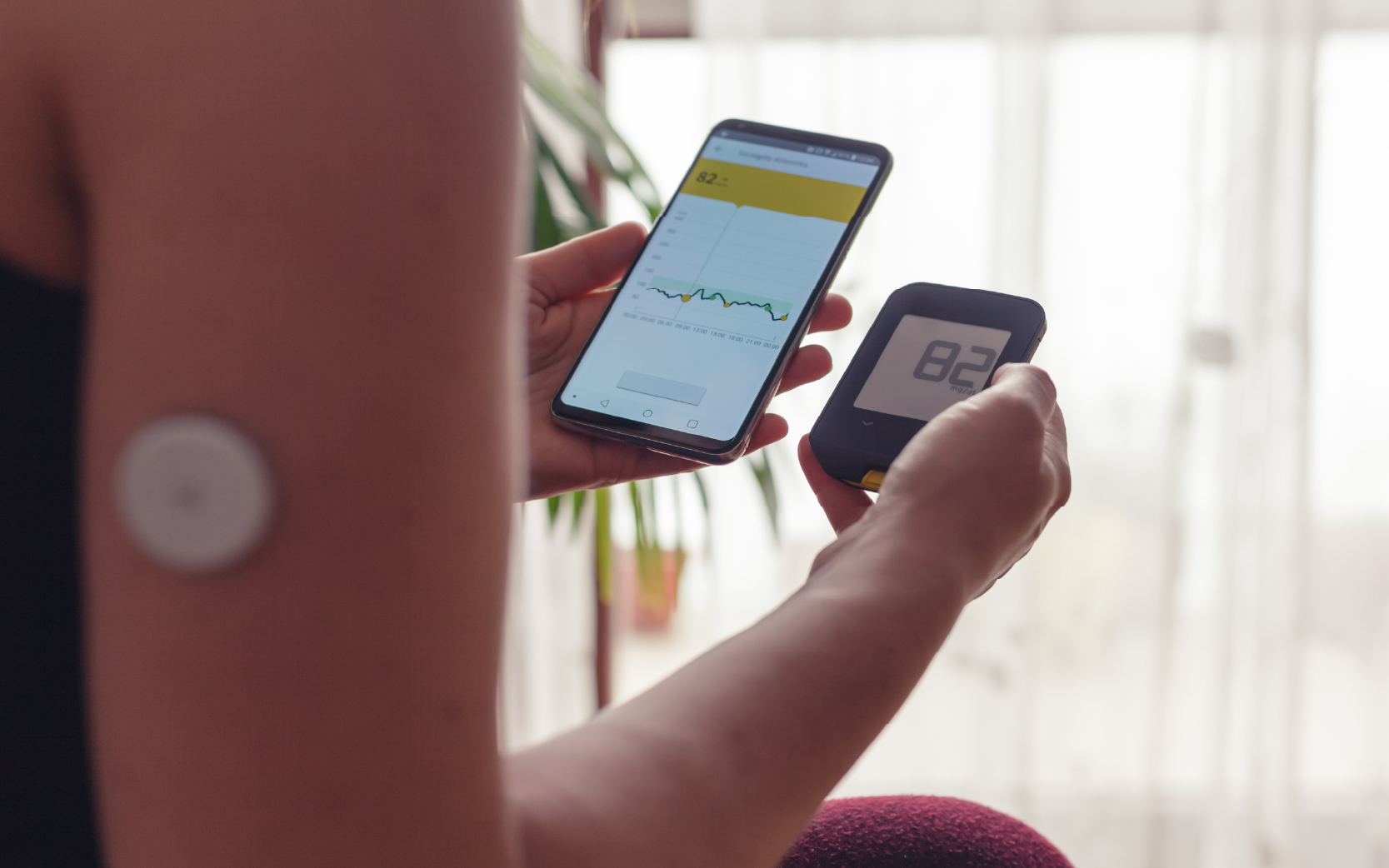 Woman comparing result of glucose level check on the traditional glucometer and on the mobile phone reading from modern technology remote sensor mounted on her arm