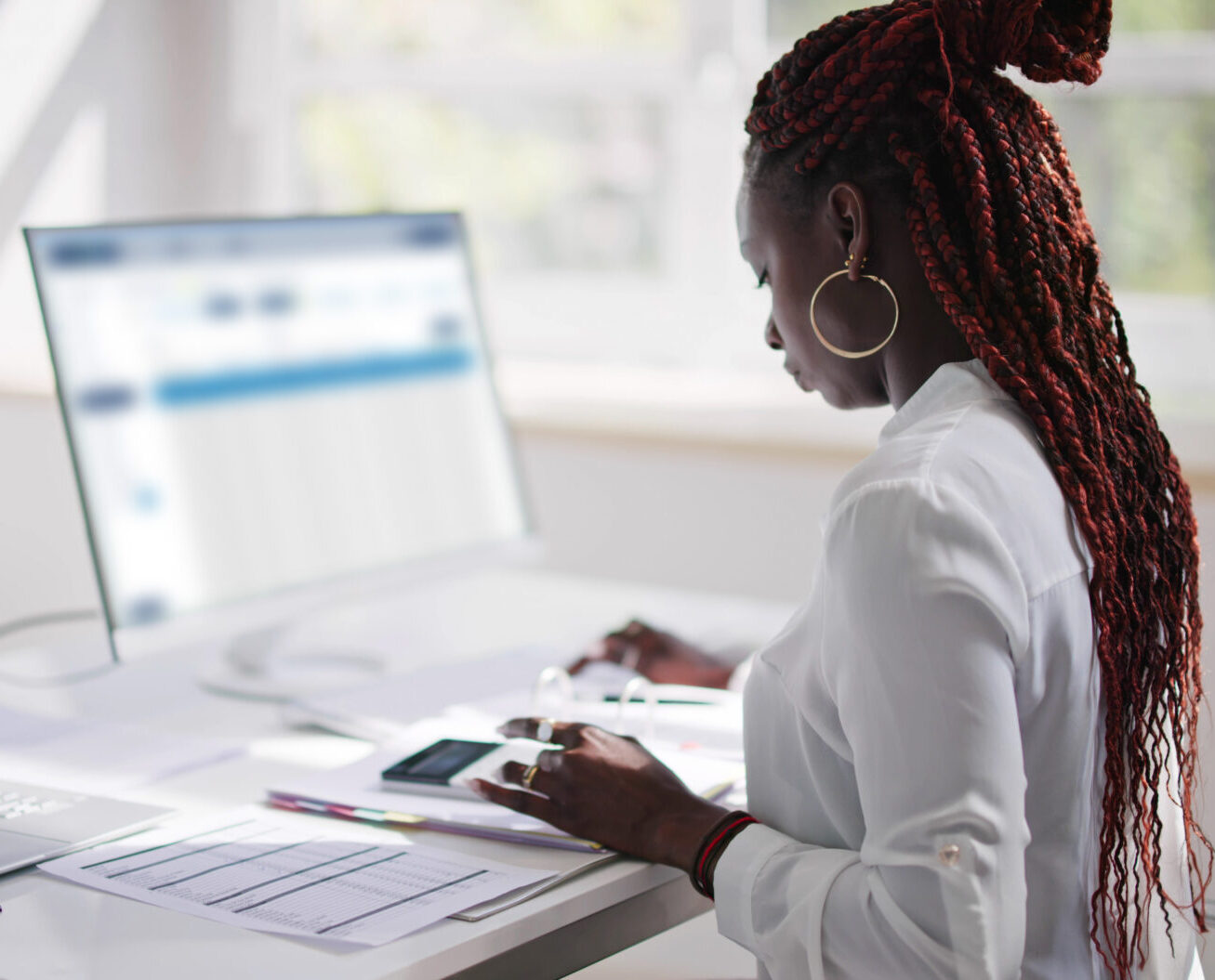 Woman sitting at her computer desk with papers and a calculator