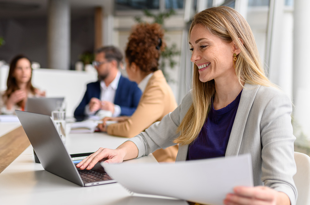 Woman at her laptop review documents smiling
