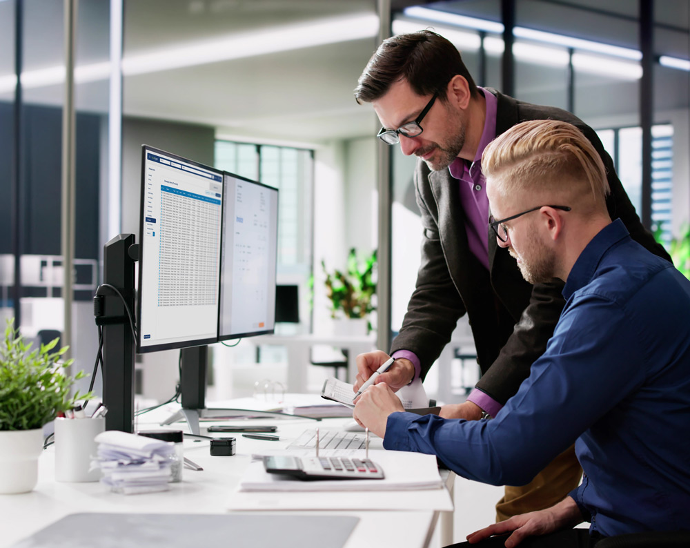 two business professionals going over documents and comparing to a computer screen