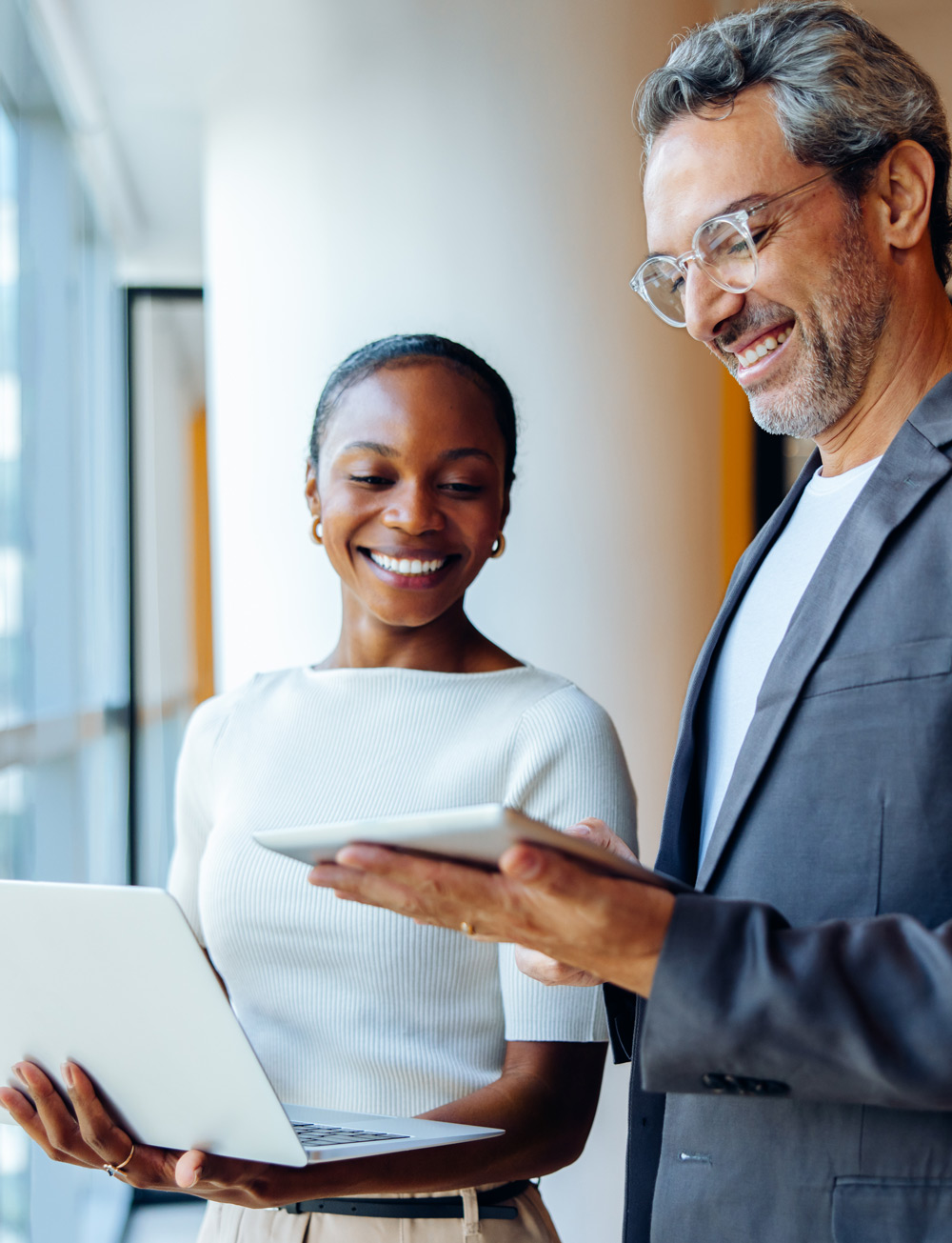 Smiling business professionals sharing ideas while working with laptops and tablets